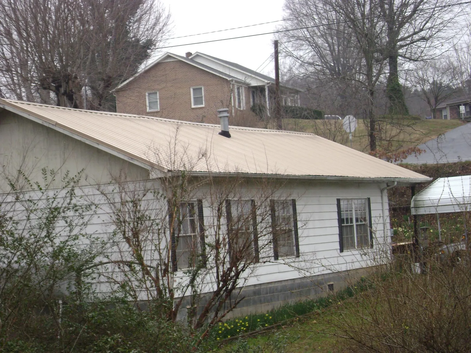 Tan metal roof on a white sided house set into a hillside — Commercial Roofing by Roofing Brothers in Bellingham